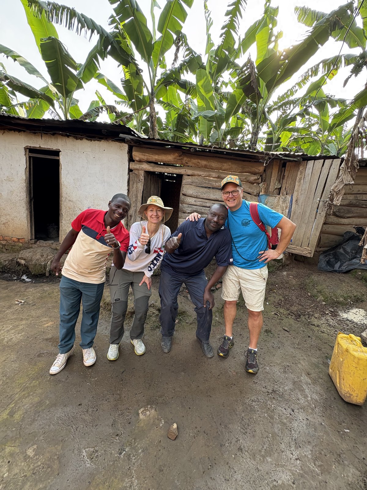 Visitors with the chicken farmer in front of his wooden farm building in Buhoma, Uganda